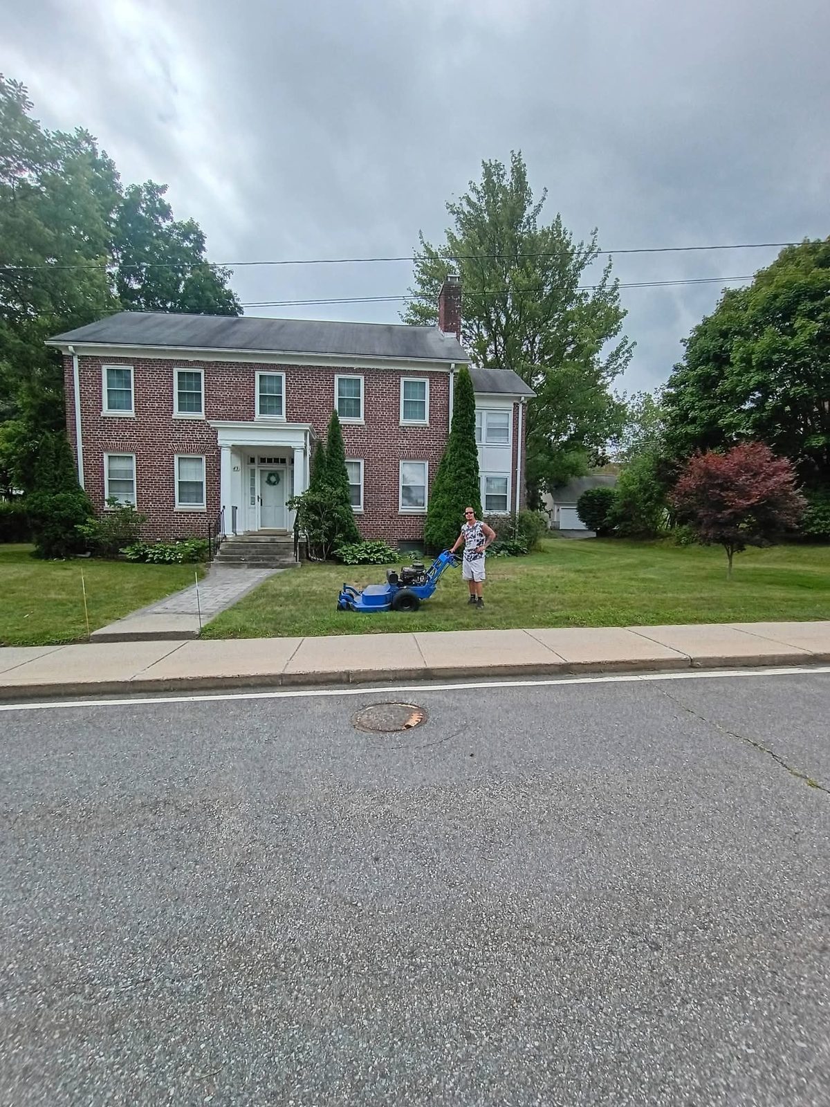Blue walk-behind mower on a fresh-cut lawn in front of a brick colonial