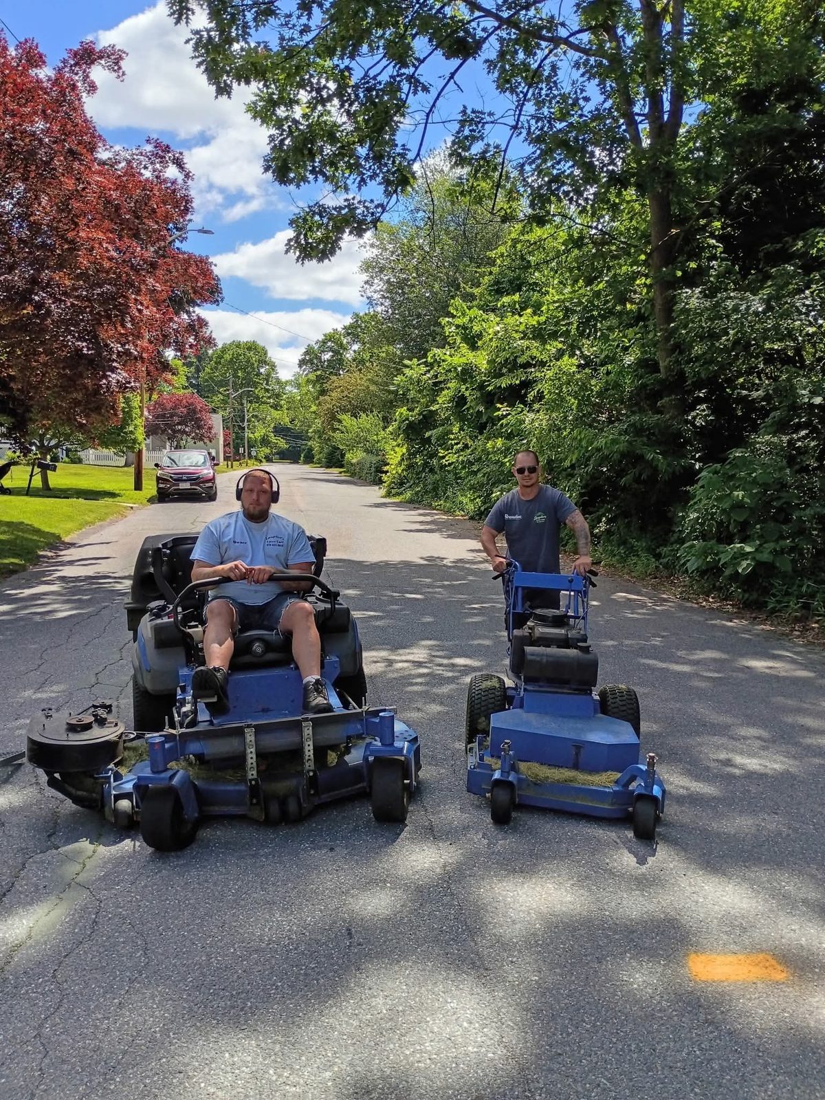 Two crew members on the blue mowers out in the street