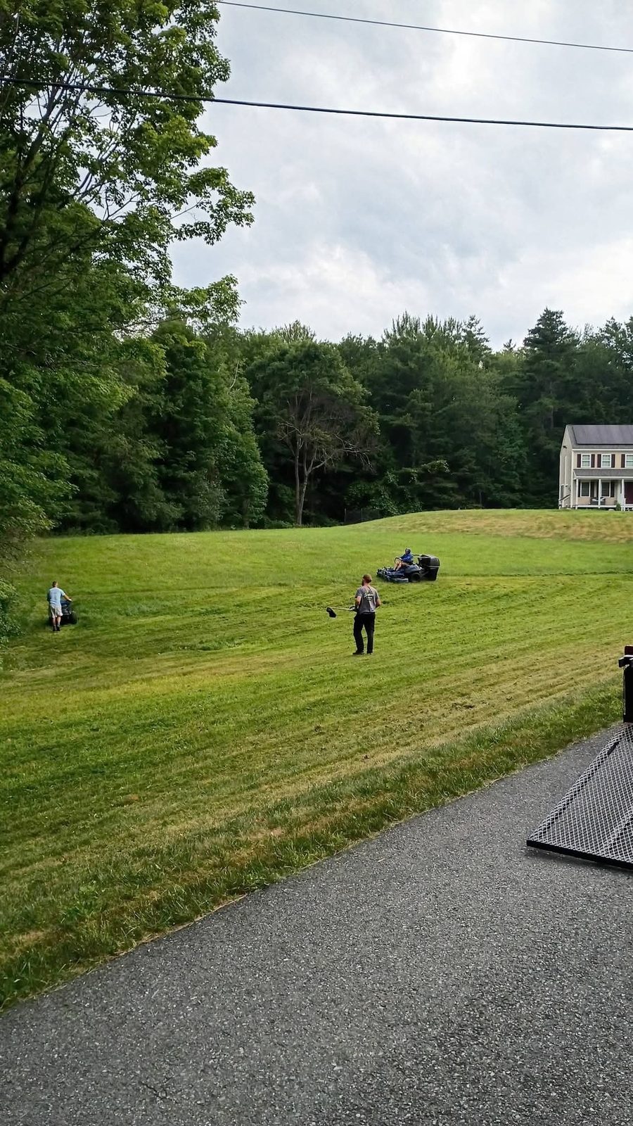 Three crew members mowing and trimming a big hillside lawn
