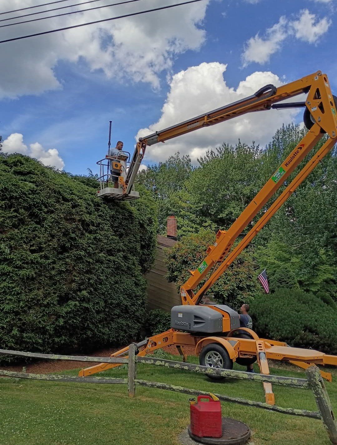 Crew trimming a two-story hedge from an orange boom lift